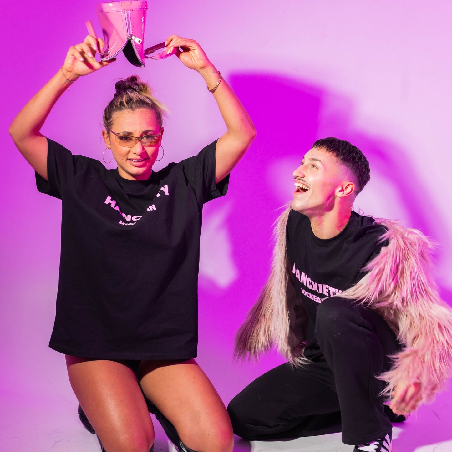Two people wearing black t-shirts with visible text, posing against a purple background.