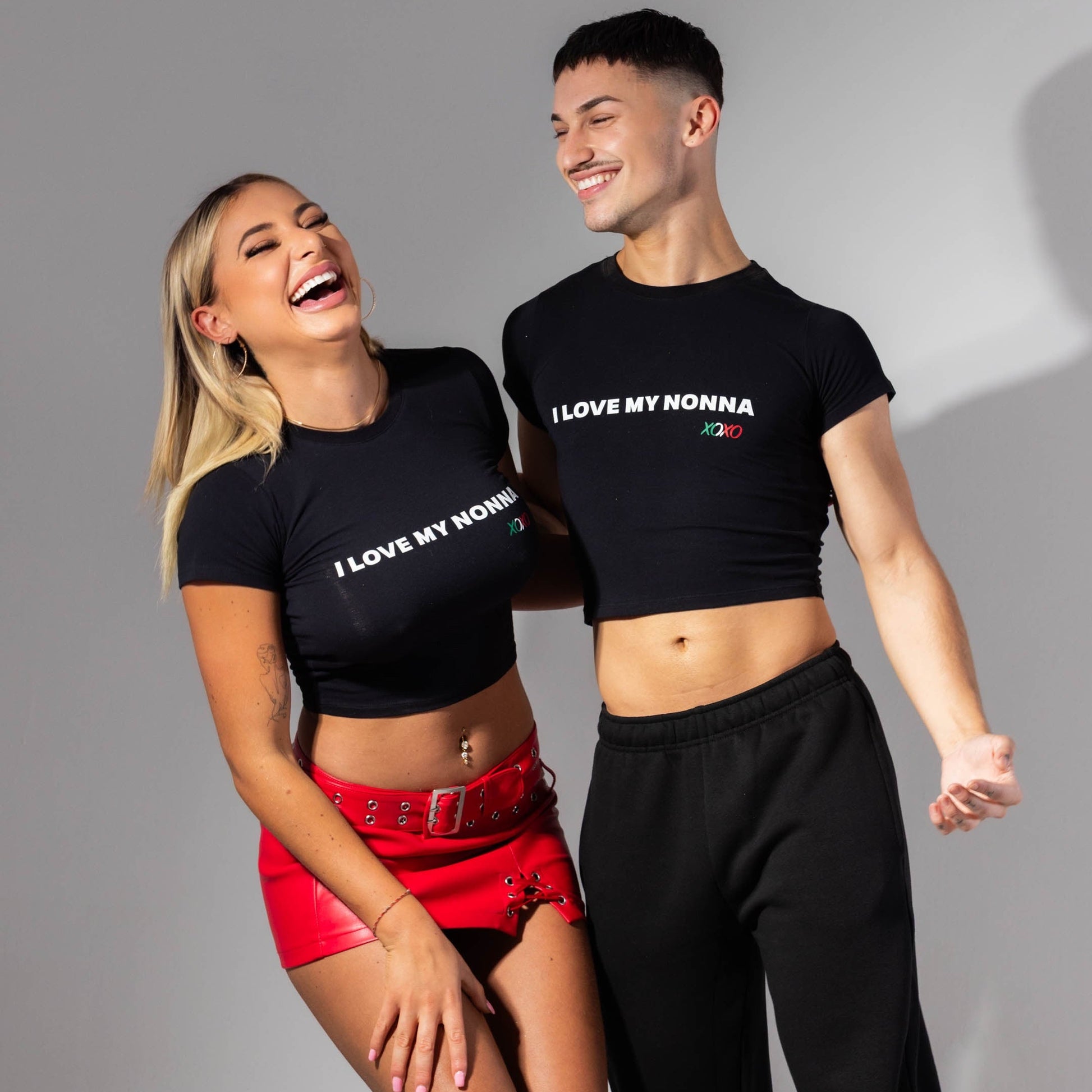 Two people wearing matching black t-shirts with text, standing against a gray background.