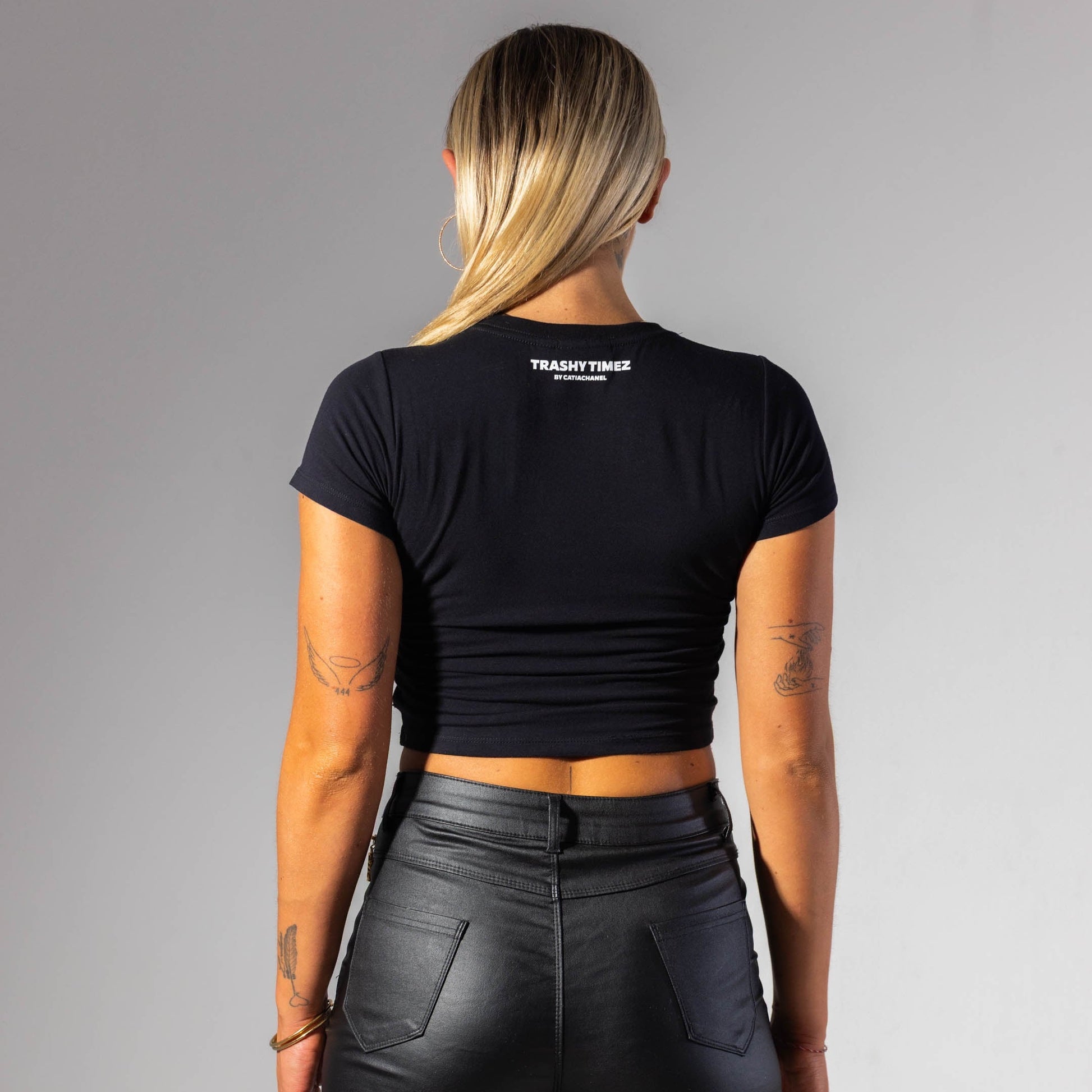 Person wearing a black crop top and leather shorts on a gray background