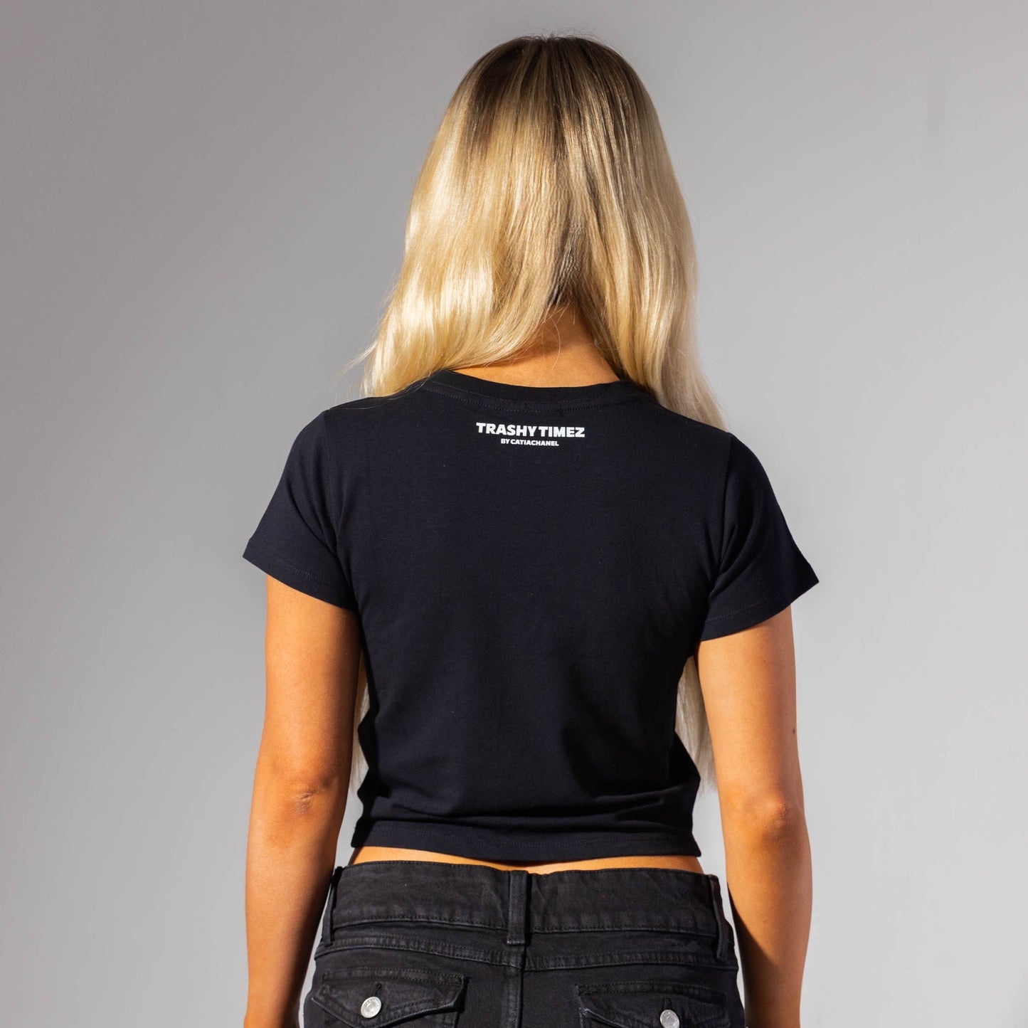 Person wearing a black t-shirt with branding on the back, standing against a gray background