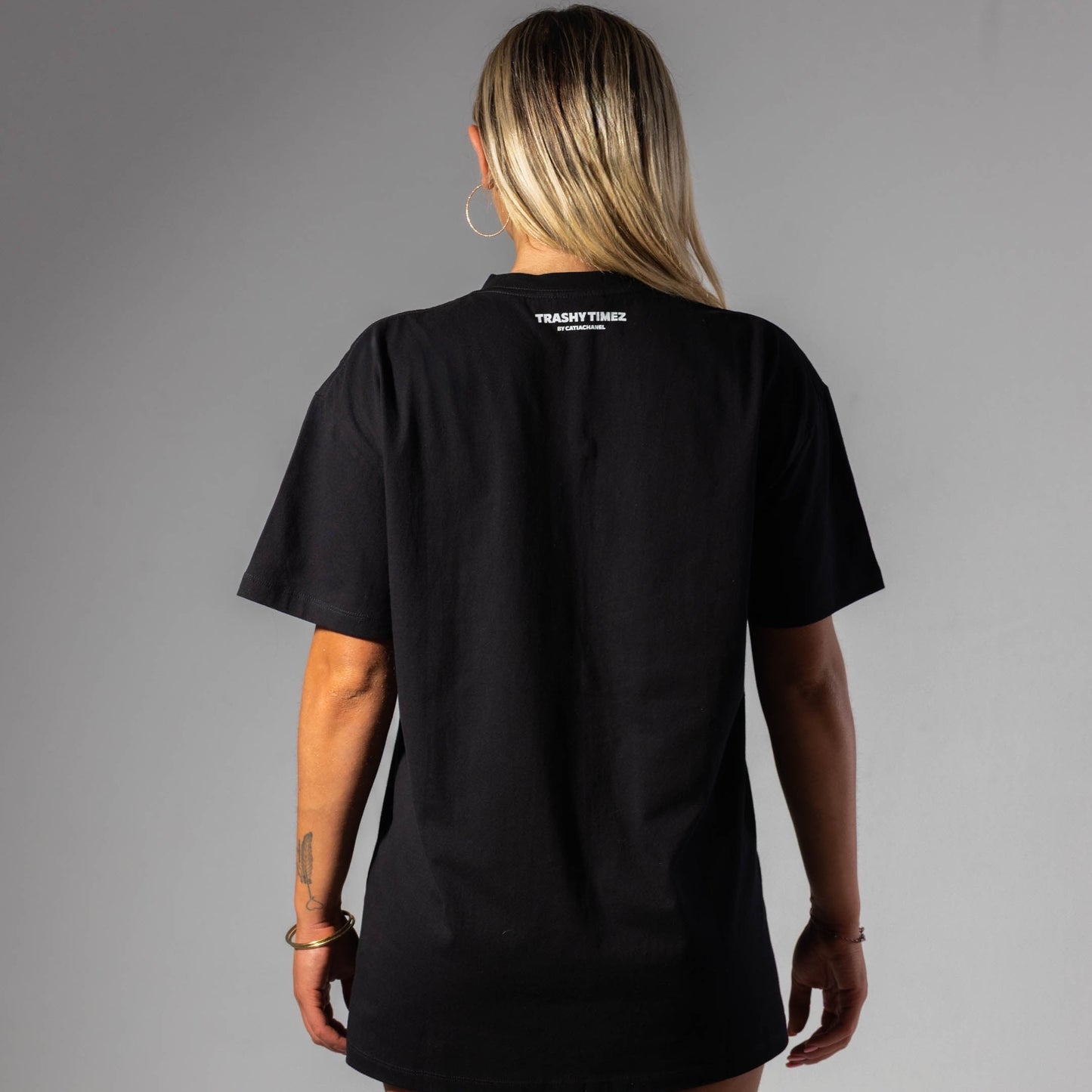 Person wearing a black t-shirt with a brand logo on the back against a gray background