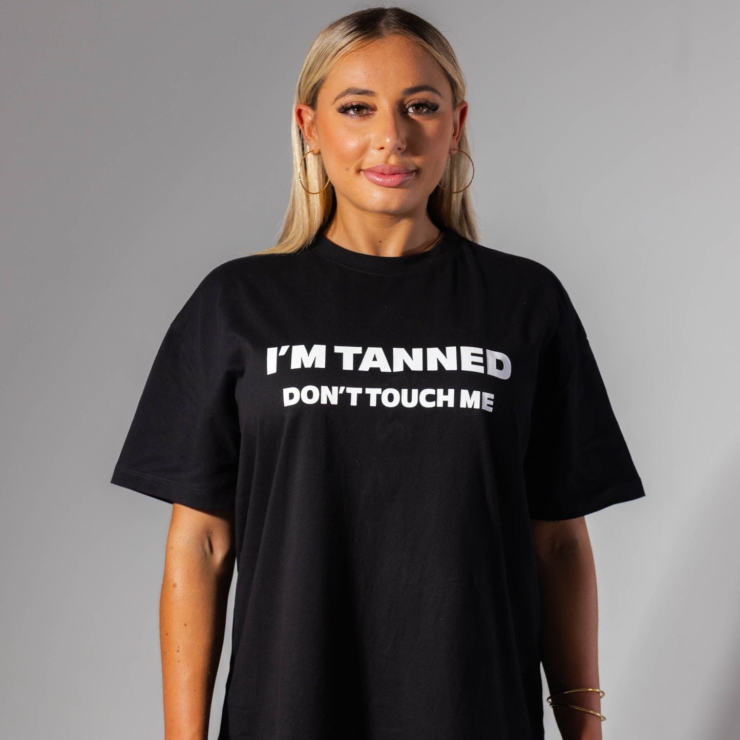 Person wearing a black t-shirt with 'I'm Tanned Don't Touch Me' text on a gray background