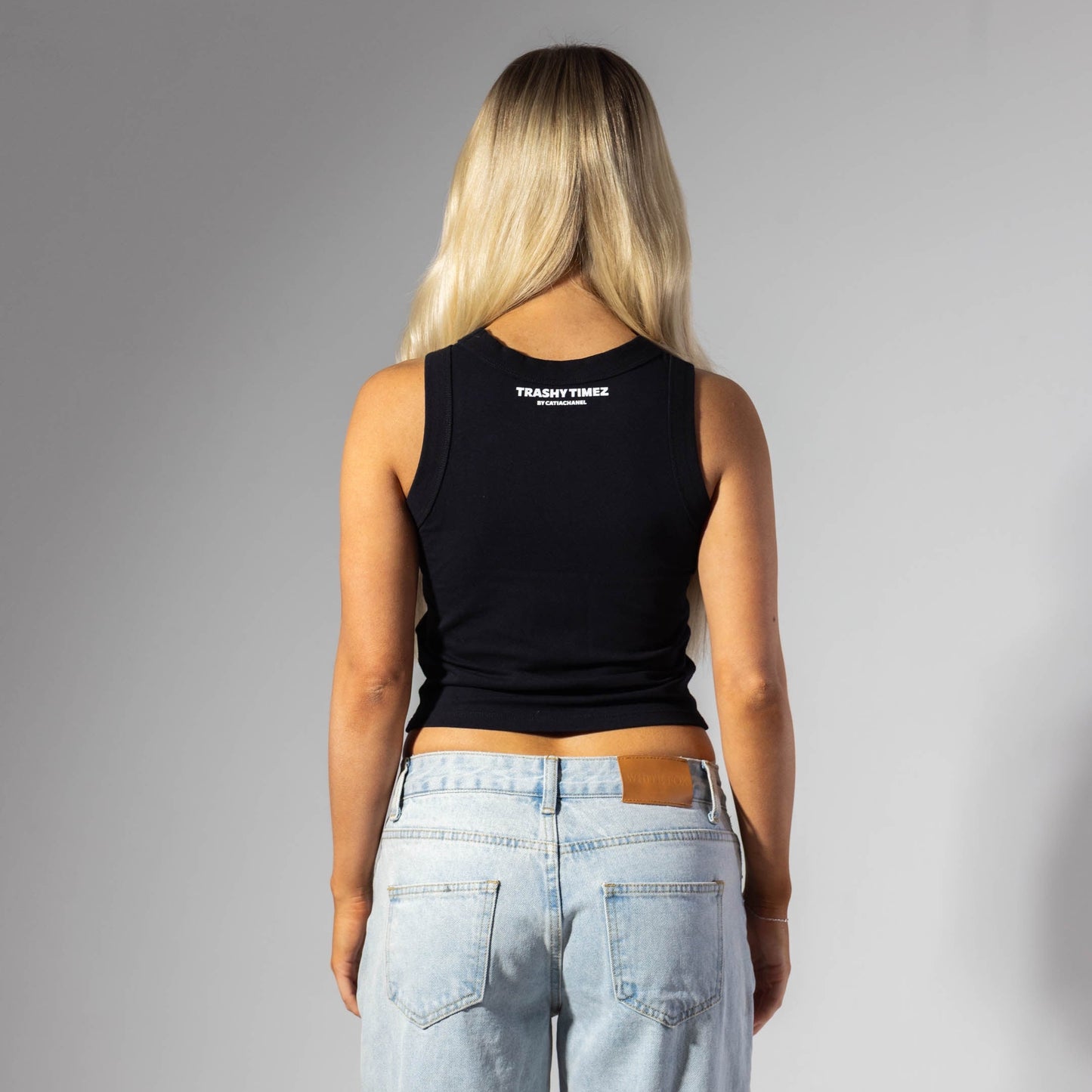 Person wearing a black tank top with a logo on the back, standing against a gray background